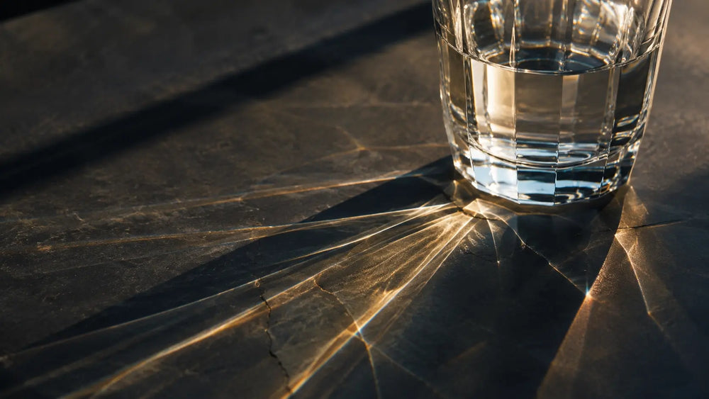 Close-up of a glass of water casting warm light reflections on a dark stone surface