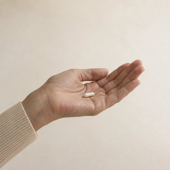 Woman’s open hand holding a single white capsule against a warm neutral background
